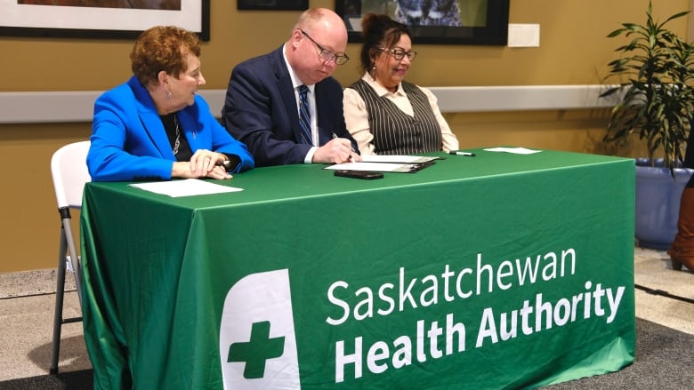 Arlene Wiks, Andrew Will and Maureen Johns are sitting at a green table and signing a document