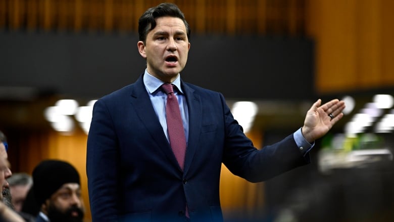 A man in a blue suit stands and gestures.