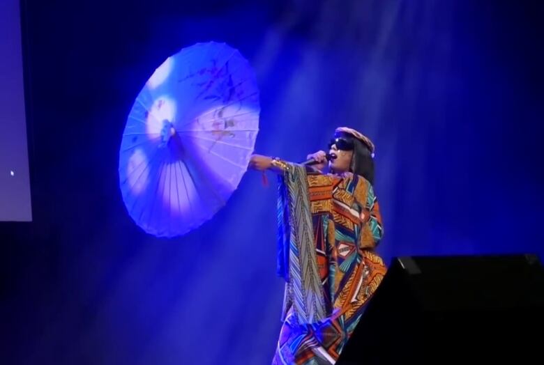 A performer in costume on stage with an umbrella.