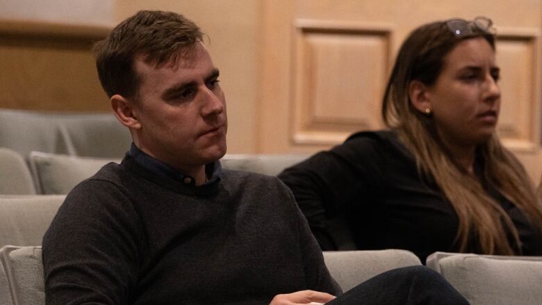 A man with a brown sweater takes notes during a meeting