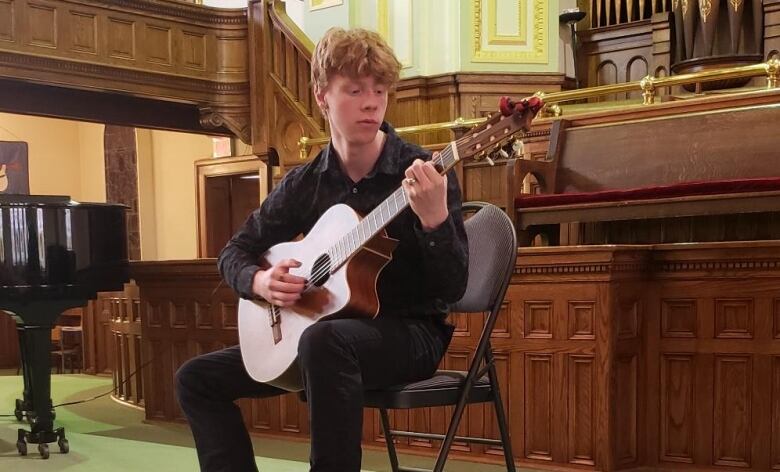 A young man performs the acoustic guitar in a church. 