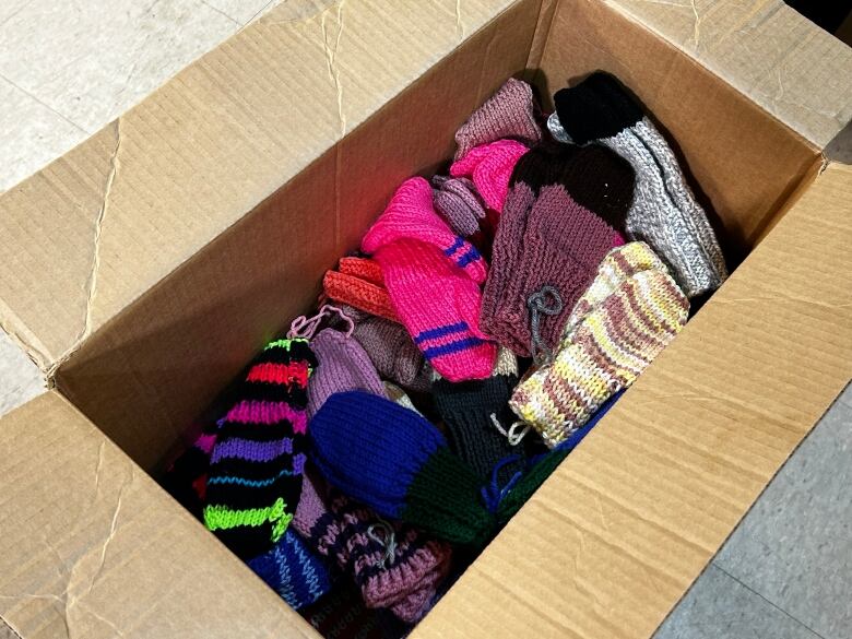 A cardboard box is filled to the brim with a colourful assortment of knitted mittens.