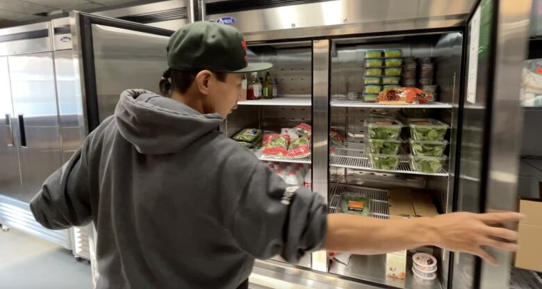 A man open a fridge full of produce.