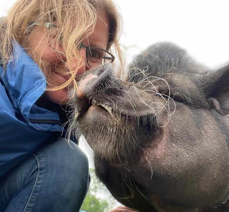 A woman crouches down to take a photo with a black pot-bellied pig.