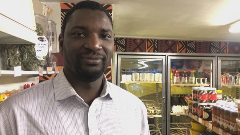 A man in a white button up shirt stands in a small grocery store. 