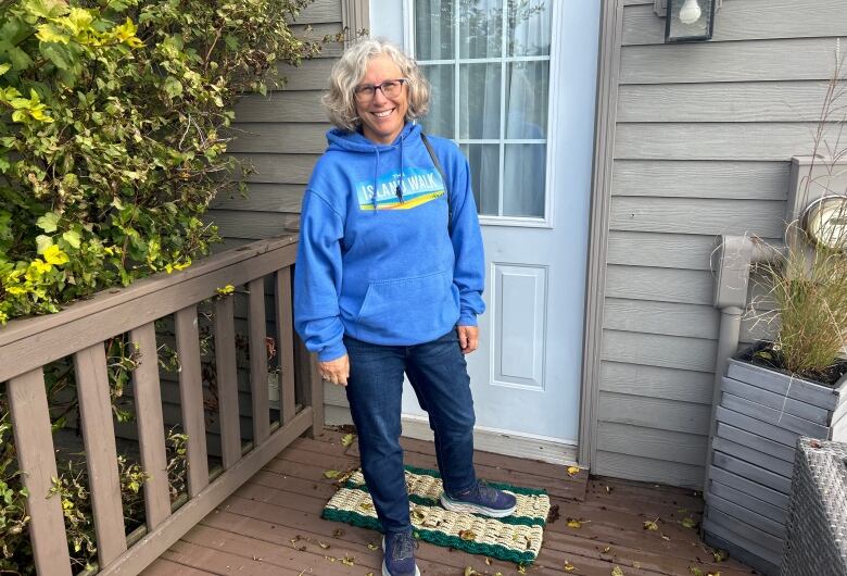 A woman in a blue sweater and jeans standing outside of a cottage.