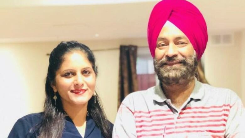 An Indian man and woman smile at the camera. The man is wearing a pink pagri (turban).