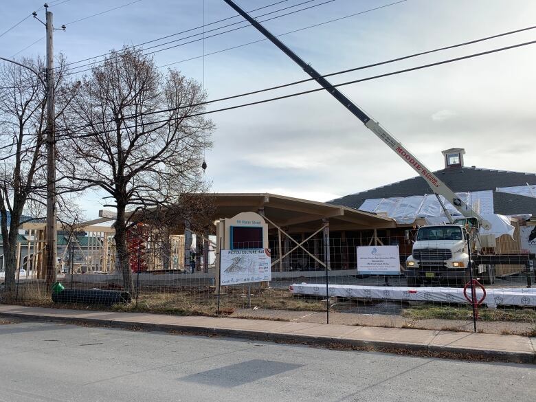 A large round building under wood frame construction. A crane is lowering material into the site. 