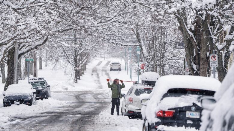 A person is shown clearing snow off their vehicle on a Halifax roadway.