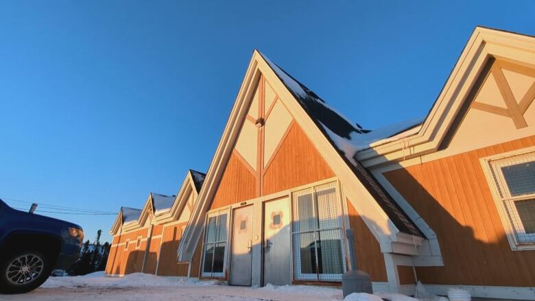 A building has triangular shapes representing trees. It's orange and white with snow on the ground below it. 