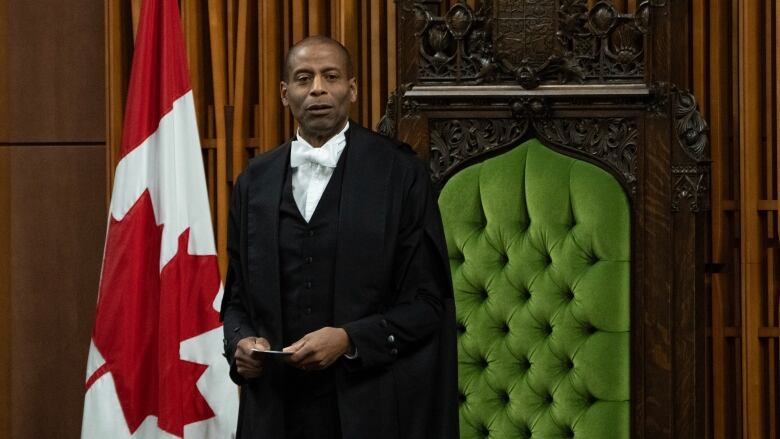 The Speaker of the House of Commons rises in his chair on the floor of the House. A Canadian flag is seen drapped beside him.