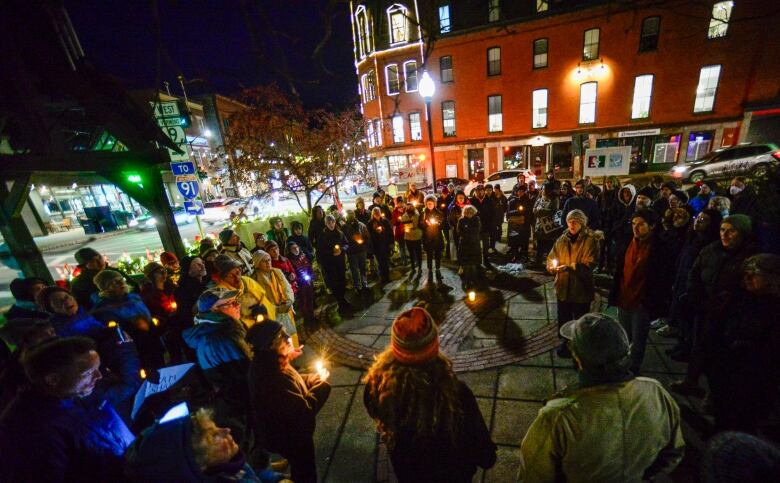 A crowd of people holding candles at an outdoor vigil at night. 