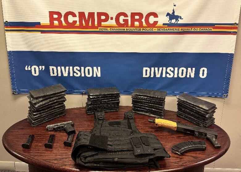 A bulletproof vest, two guns and several small black rectangles arranged on a table. A police banner is behind it.