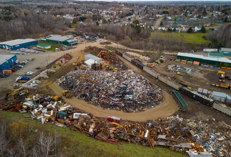 A large pile of scrap material with residential properties in the background.