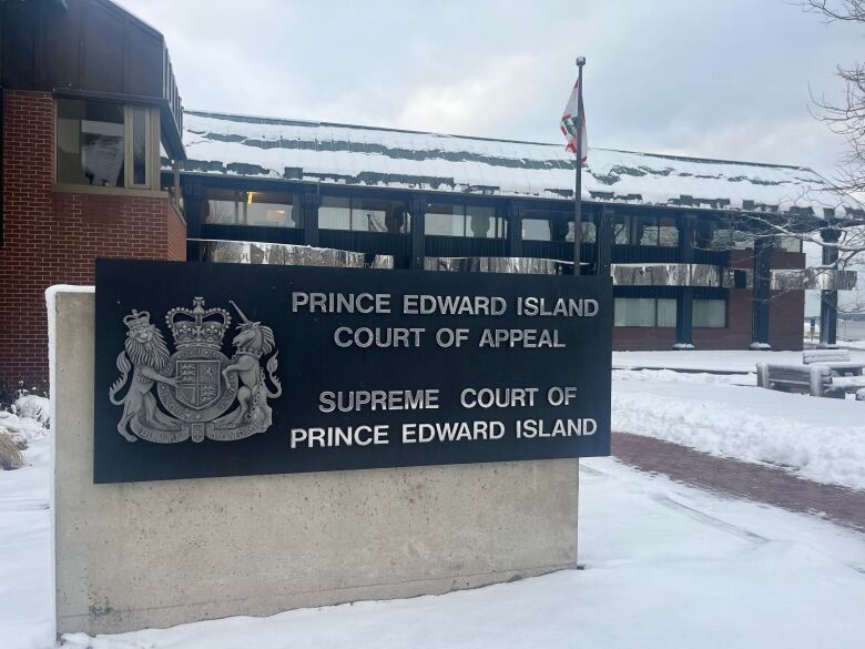 Snow covers an open area in front of a brick building with a sign saying 