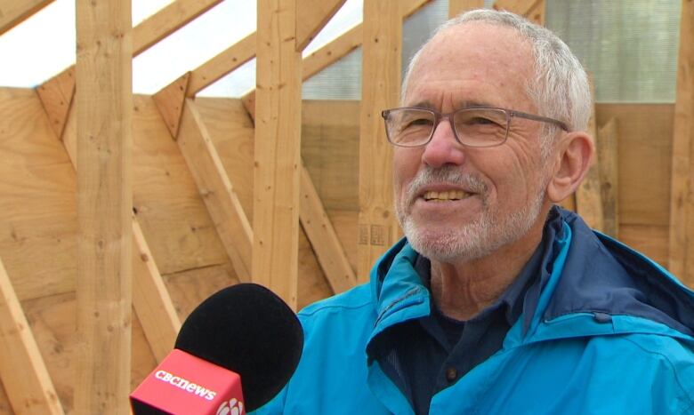 An older bearded man smiles while wearing a blue windbreaker 