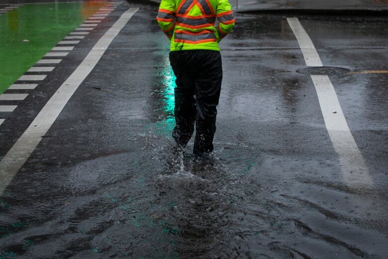 A person wearing a high-vis shirt wades through a puddle amid heavy rain.