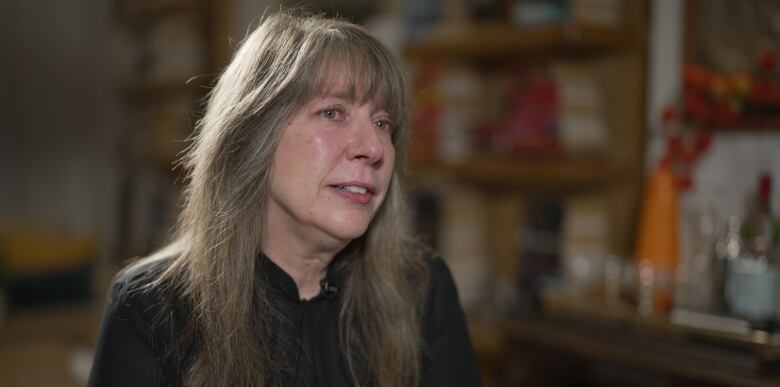 A woman with long hair and wearing a dark sweater has a serious expression on her face as she talks to someone who can't be seen in the photo.