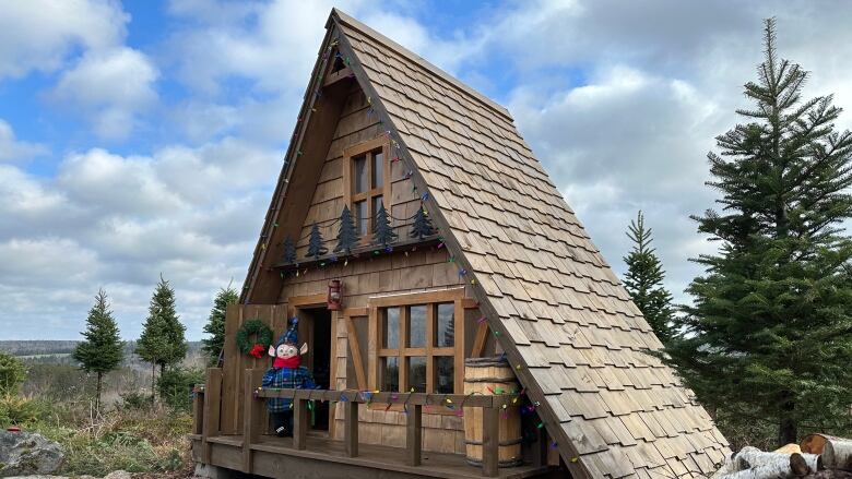 a plush elf stands on the door step of an a frame chalet 