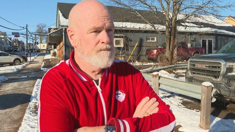 Bald man with red sweater standing on street.