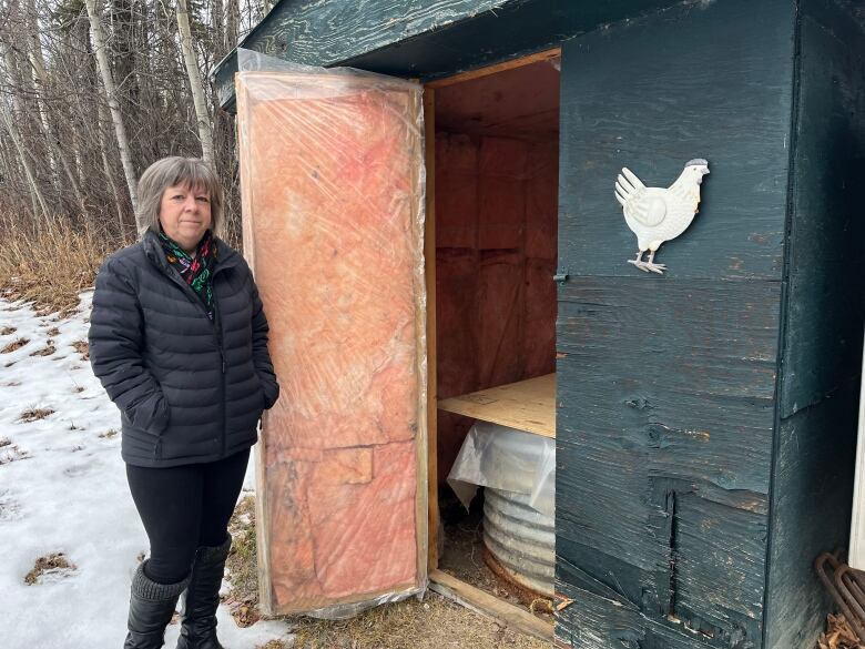 Woman stands by an out building for her well