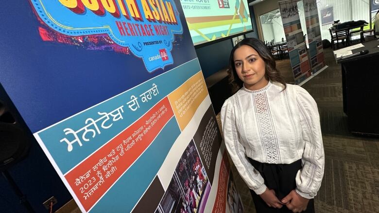 A woman stands beside a sign saying South Asian Heritage Night.