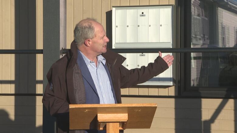 Ernie Hudson stands outside at a podium during an announcement in Alberton. He is pointing to the building behind him. 