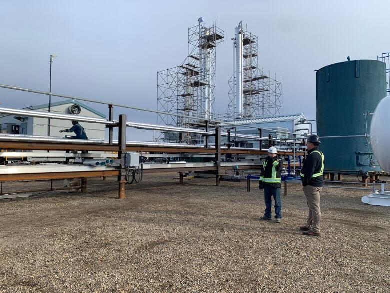 Two men in high-visibility clothing and hard hats observe the helium purification plant owned by Royal Helium near Brooks, Alta. 