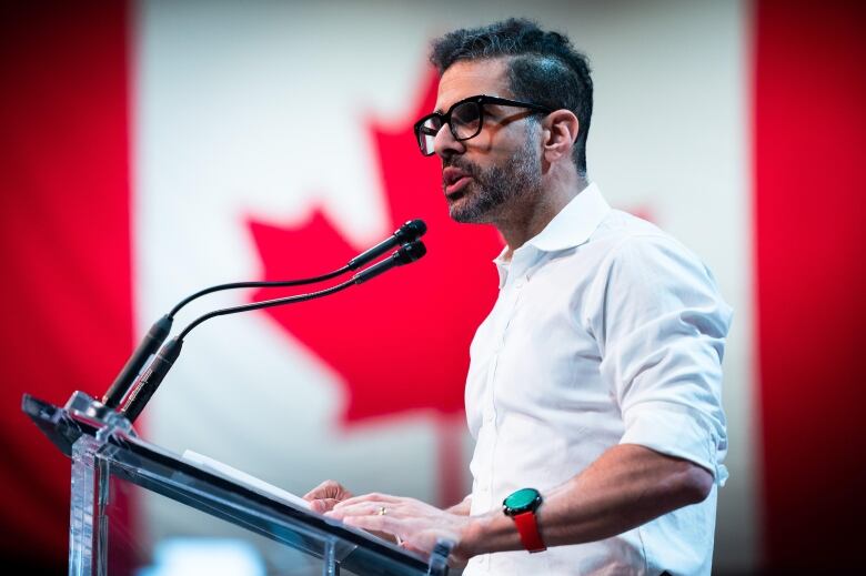 A man speaking at a mic in front of a Canadian flag. 