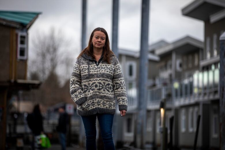 A woman in a cowichan sweater walks along a dock with floathomes in the background.