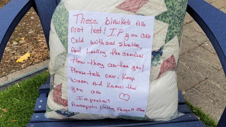 A plastic bag containing a quilt sits on a outdoor lawn chair. There's a kind note attached to the bag.