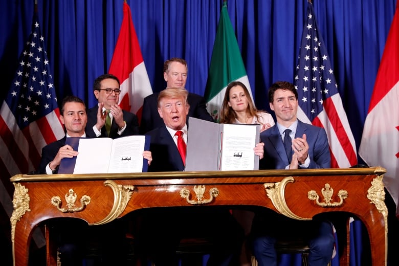 Leaders Donald Trump, Justin Trudeau, and Enrique Pena Nieto hold up leather-bound copies of their signatures, with officials in the background.