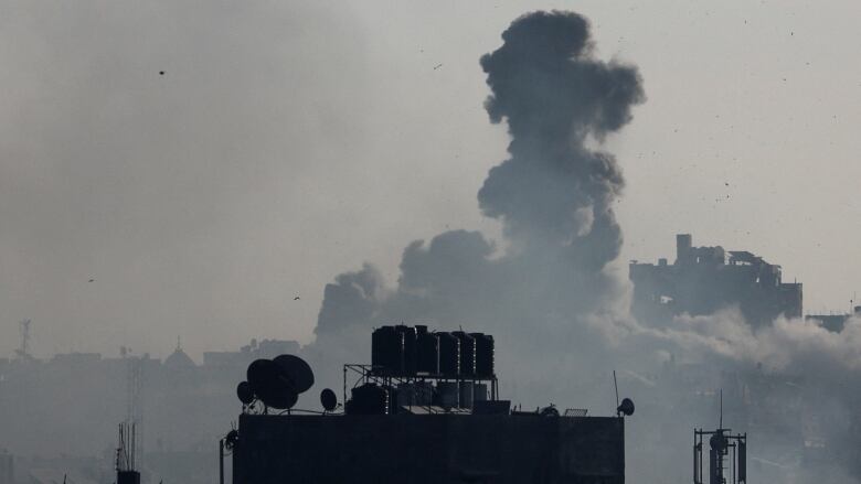 Smoke rises behind buildings following a military strike.