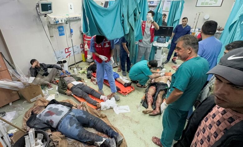 Wounded people lie on the floor of a medical establishment, as doctors in blue scrubs attend to them.