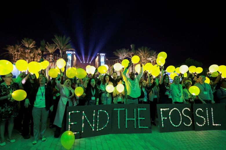 Protesters hold yellow orbs at night in front of a sign that says 