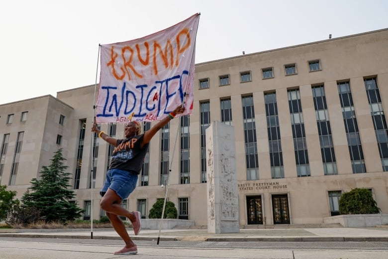 Woman dancing, holding sign in front of court building: Trump Indicted