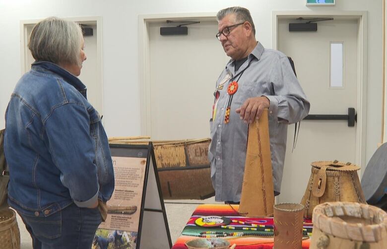 Elder Junior Peter-Paul stand in front of a canoe on display speaking with a woman during the fall favours festival.