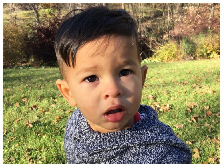 A boy sits outside on the grass and looks questioningly at the camera.