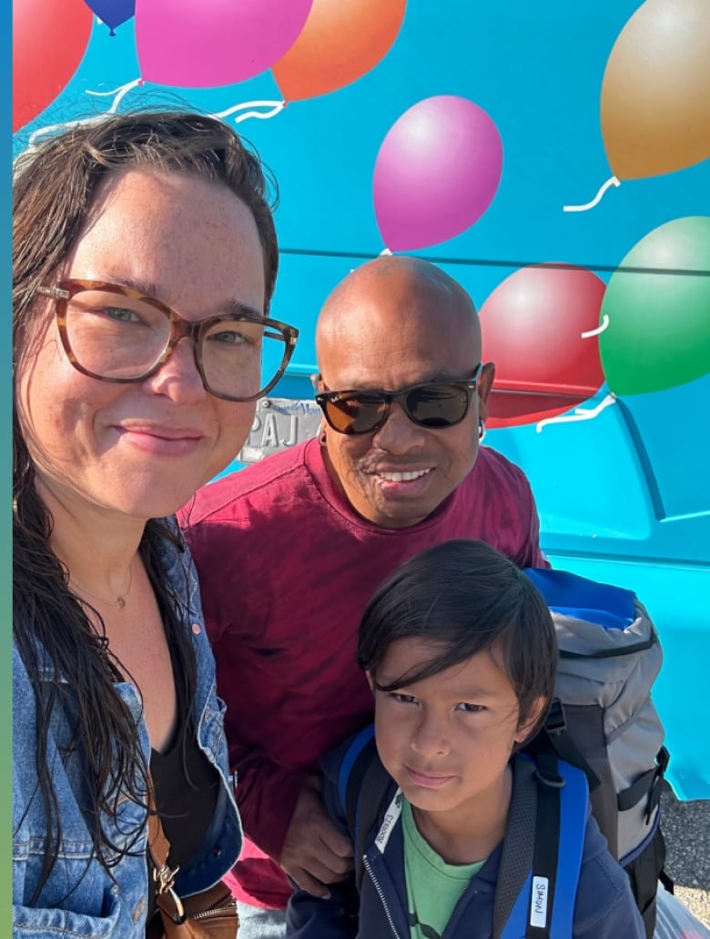 A woman and man look at the camera with small smiles as a boy with a backpack stares at the camera. 