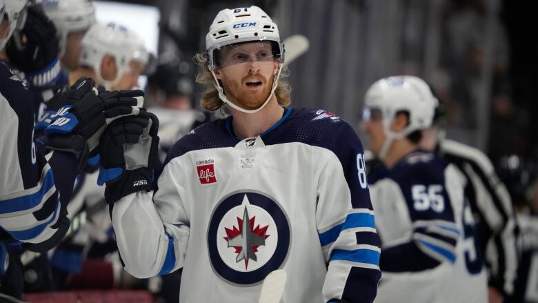 Player in Winnipeg Jets jersey high-fives players on the team's bench.