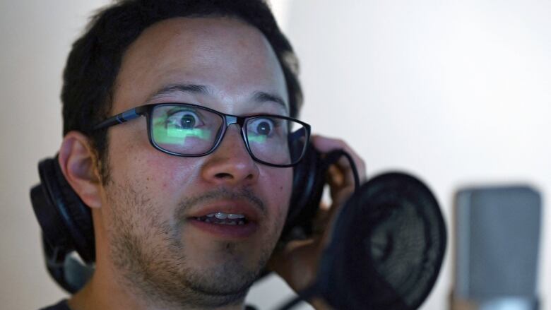 A man speaks into a microphone while watching the screen in front of him. 