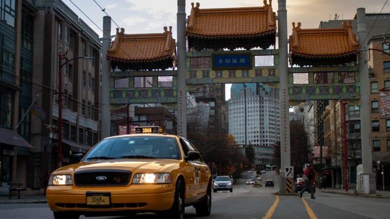 A yellow new york taxi cab is pictured driving beneath the iconic Vancouver Chinatown gate.