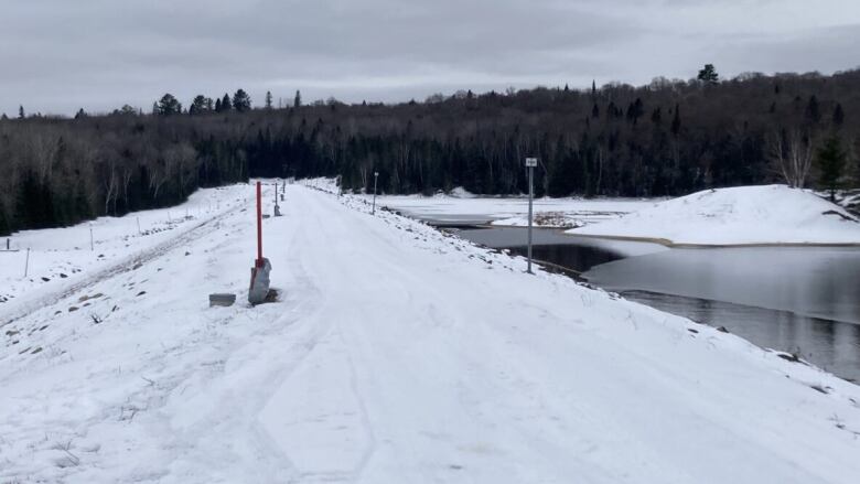 A snow-covered road atop a dike, with a body of water on one side.