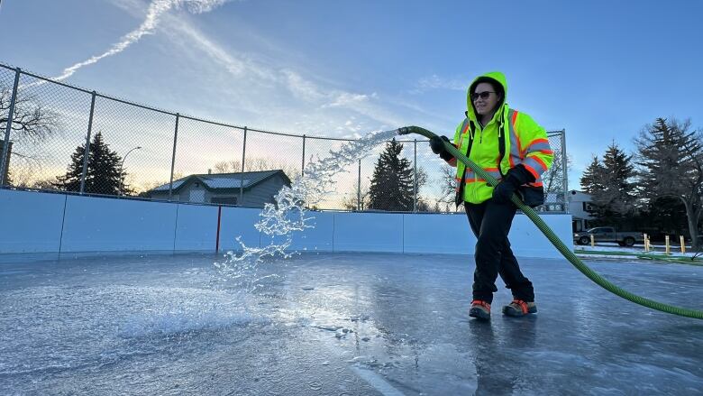 A city employee floods an outdoor rink with a hose of water.