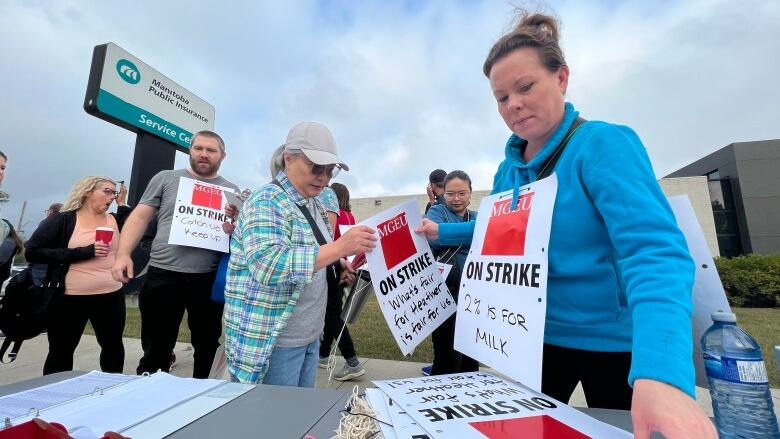 Striking workers, walking on a sidewalk, approach a table to pick up supplies