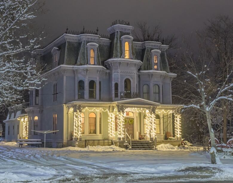 A large house decorated with Christmas lights with a light dusting of snow. 