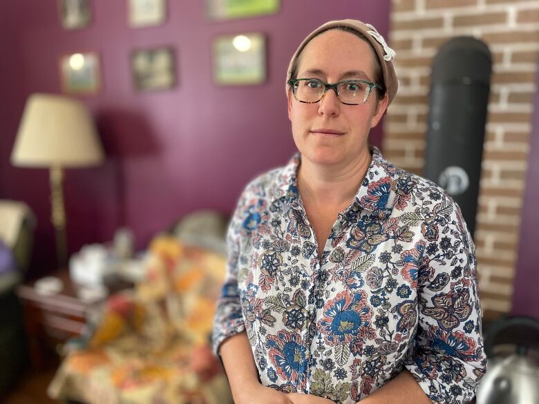 A woman in a floral shirt stands in the living room of a home. 