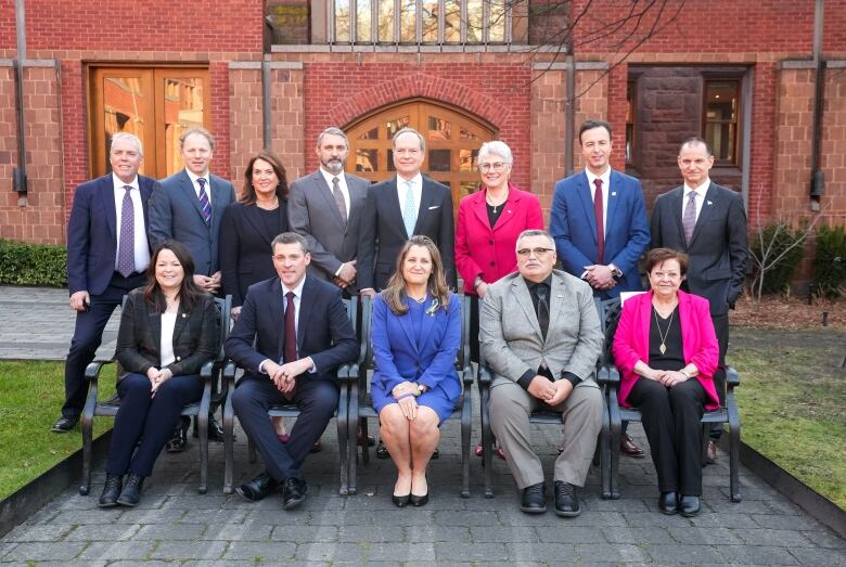 The provincial finance ministers pose for a group photo with the federal finance ministers outside of a brick building.