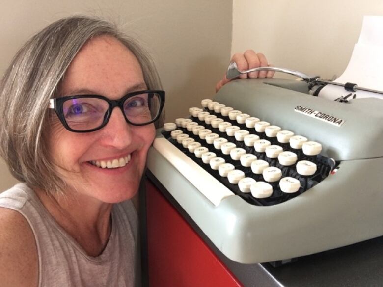 A woman is smiling inf ront of a typewriter. 