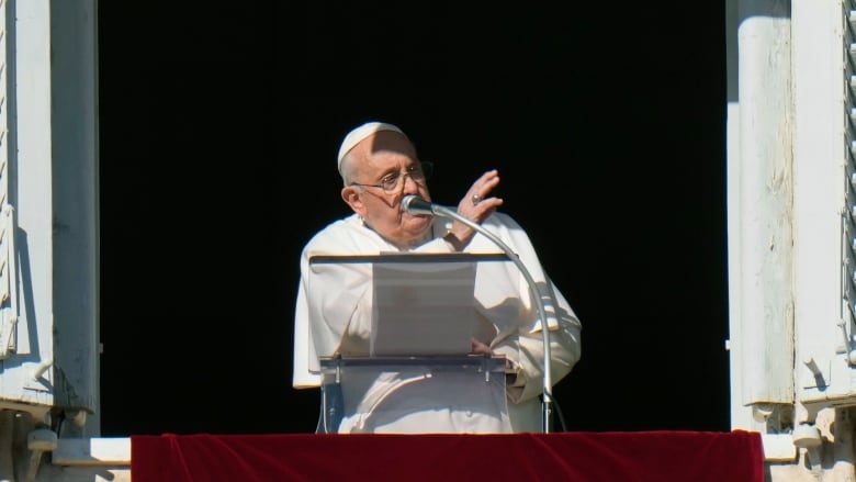 A bespectacled man in white religious garments speaks from an open window.